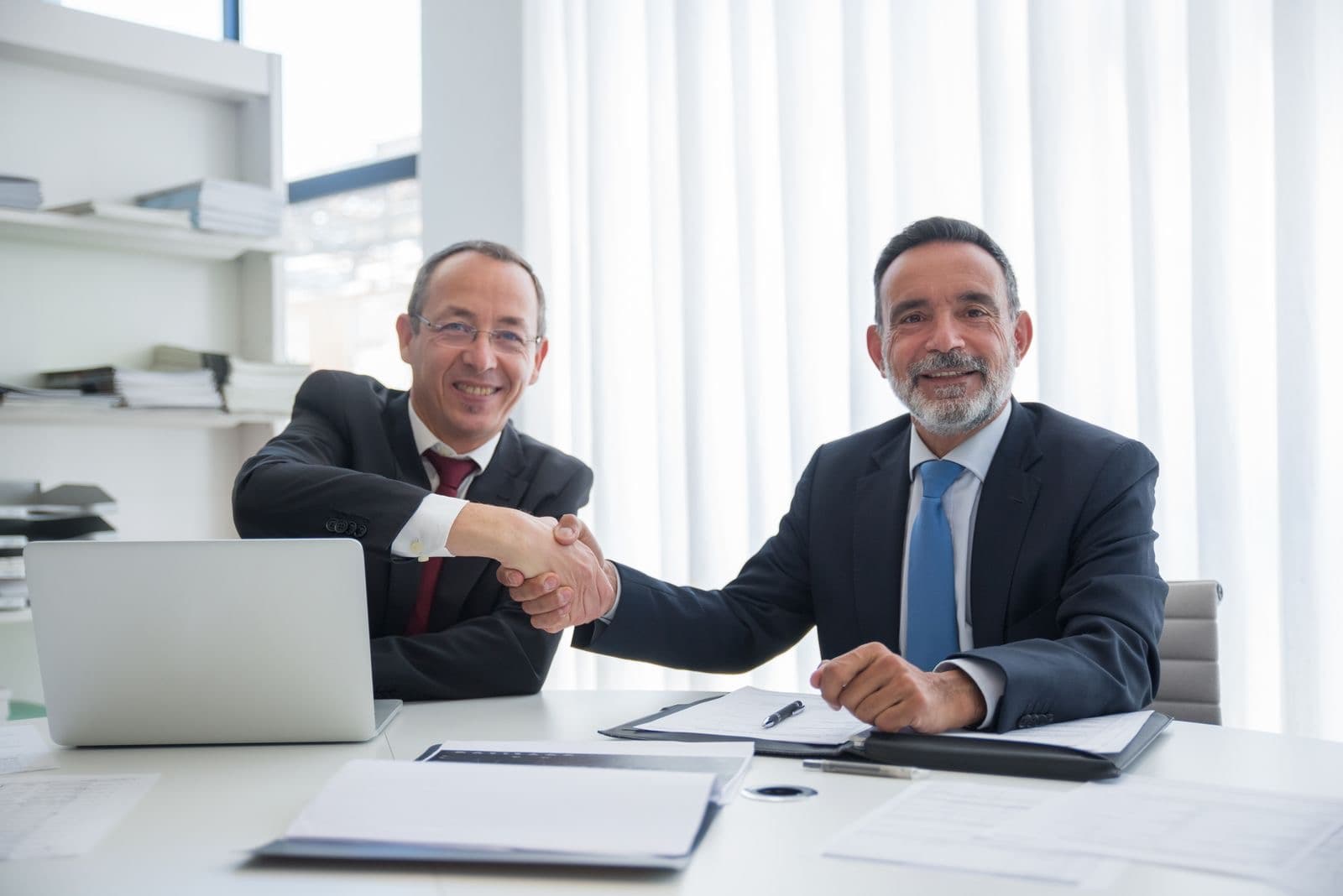 Two executives shaking hands over a desk